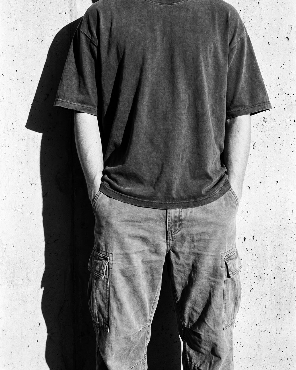 Cropped torso shot of an oversized washed-black tee and cargo pants against a concrete wall