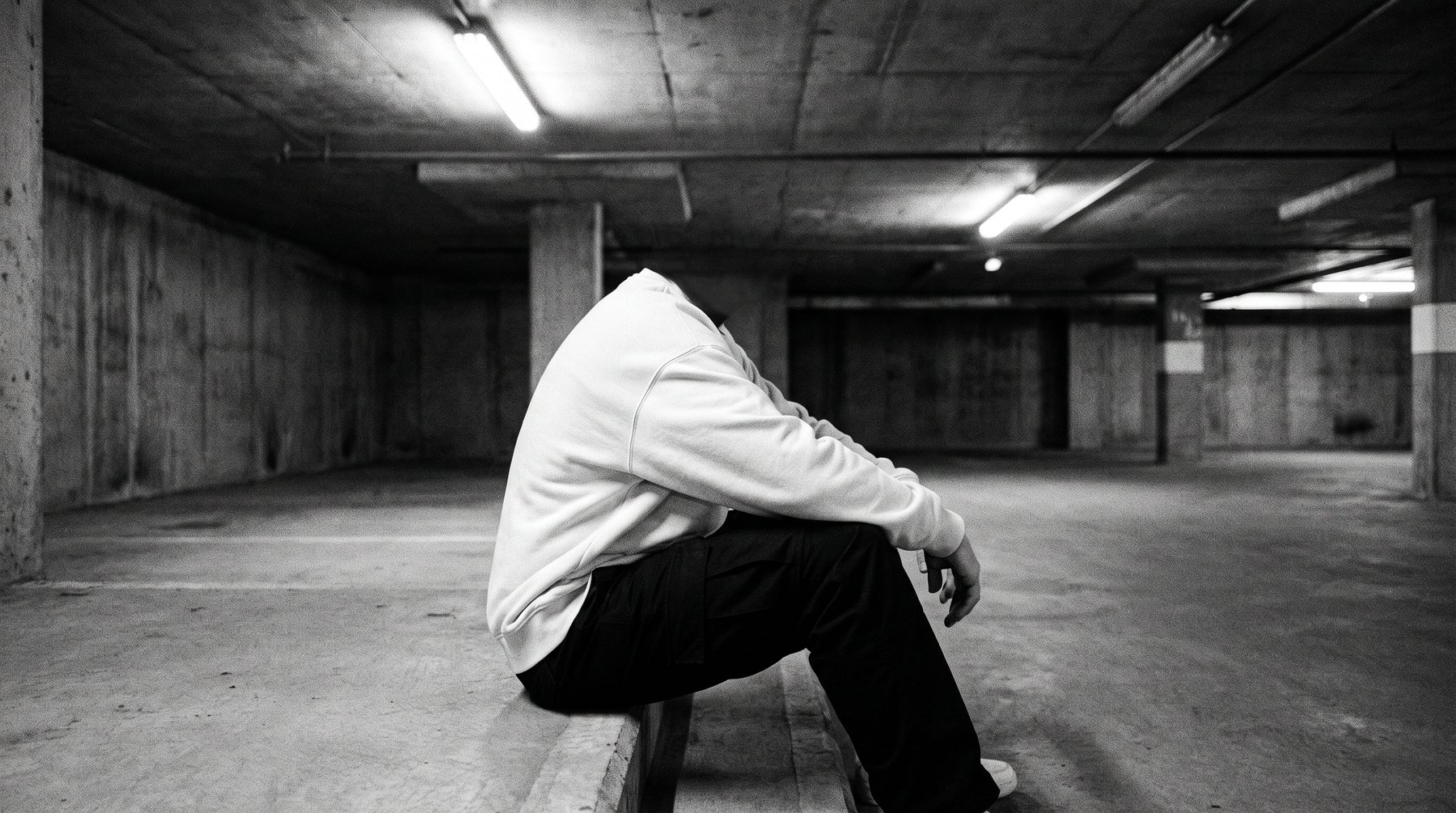 Person in bone crewneck seated in an empty parking structure